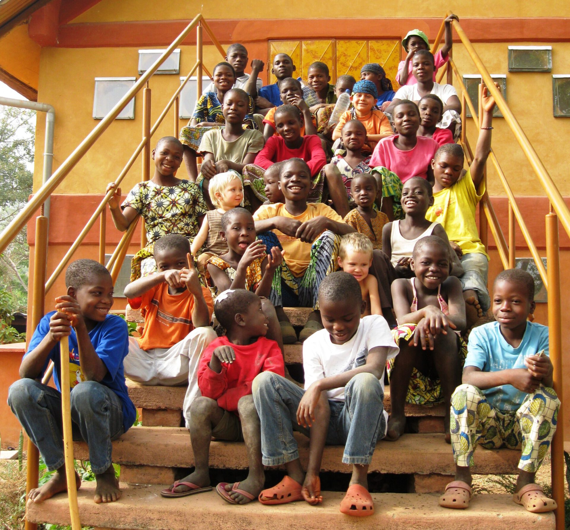 30 Kinder sitze n auf einer Treppe, vor einem orange - gelb gestrichenen Gebäude