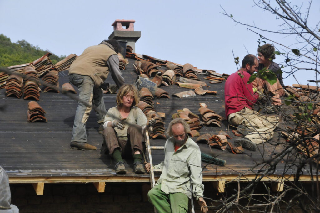 Mehrere Menschen decken ein Dach voll Ziegel ab