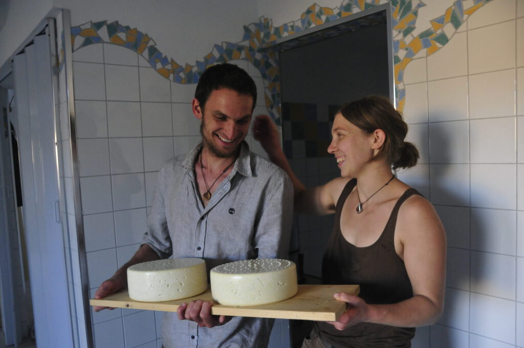Mann und Frau präsentieren selbstgemachte Käselaiber in einer Käaserei