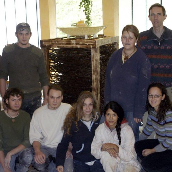 Gruppenfoto Heidehaus Gruppenbild Vor einem kleineren Zimmerbrunnen mit 11 Leuten